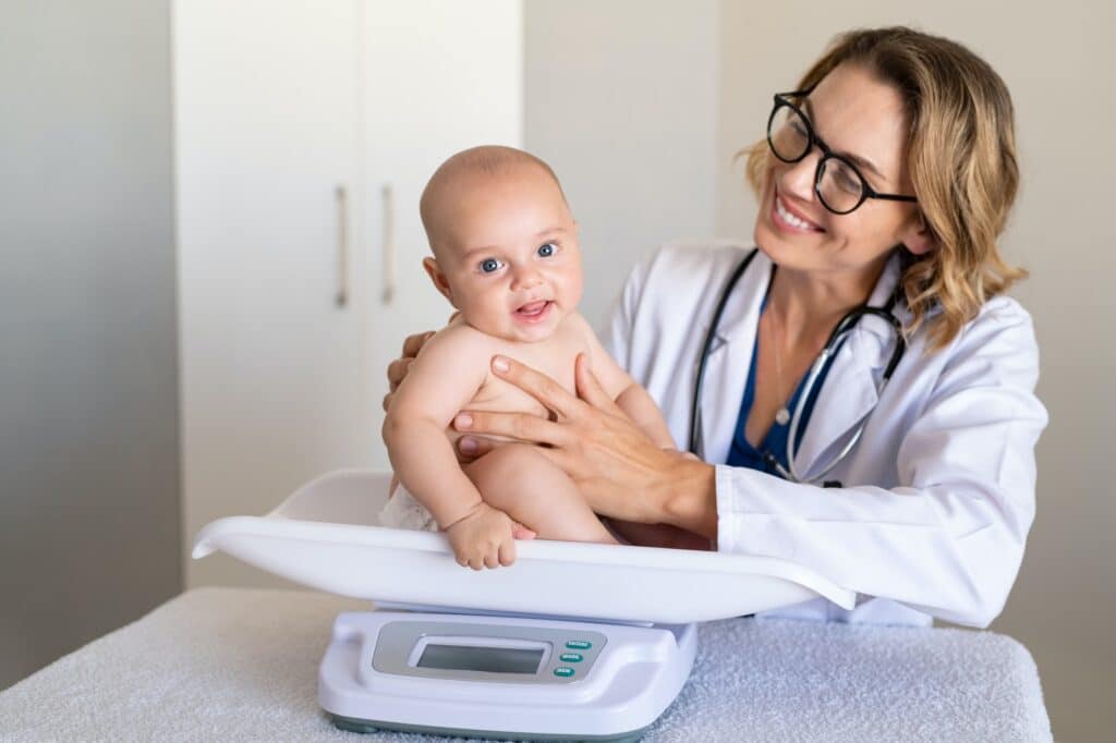 Smiling pediatrician weighing cute baby